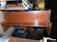 Side angle view of the long wooden church pew showing its length and polished wood surface with some wear marks.