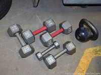 Overview of dumbbells including 20 lb, 25 lb weights, and kettlebell positioned on concrete floor with visible wear.