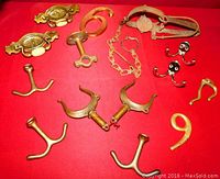 Various metal objects including hooks, antique key, decorative handle with ceramic inlays, faucet handles, chain and trap device arranged on red background.