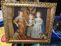 Full view of the needlepoint art showing three children and two dogs in an ornate gold-colored frame.