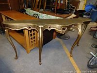 Front and side angled view of gold tone sofa table showing scalloped edges, floral carved details, and cabriole legs.