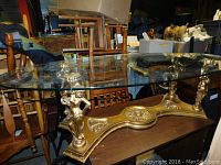 Overall view of the coffee table showing the oval glass top and gold metal base with sculpted female figures.