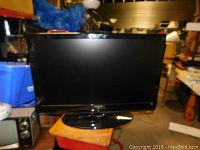 Front view of Samsung large flat screen TV on stand, showing clean screen and base.