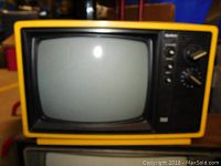 Front view of small yellow portable CRT TV showing screen and control knobs.