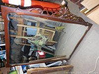 Full view of the large wood framed mirror with top decorative carvings including lattice and shell motif.