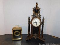 Photo showing two decorative clocks, one small brass carriage clock and one larger ornate wooden mantel clock