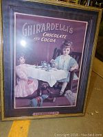 Framed vintage-style Ghirardelli's Chocolate and Cocoa print featuring two children sitting at a tea table with toys and dogs beneath.
