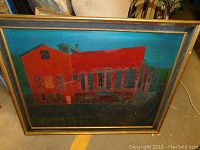 Framed painting showing a red building with multiple windows and roof parts, against blue and green background.