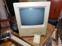 Front view of vintage Apple Macintosh SE/30 computer with built-in CRT monitor and original mouse placed in front.