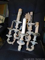 Large antique metal wall sconce with five candle holders shown against black chair background, visible aging and patina, wax residue on candle holders.