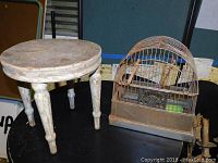 Wooden milk stool with worn paint and rustic, vintage condition shown next to the wire birdcage on a table.