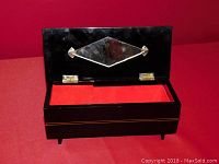 Open view of the music box showing the red fabric lining inside and diamond-shaped mirror attached to the interior lid.