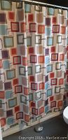 Shower curtain hanging on a rod, showing full pattern with multicolored squares and attached rings