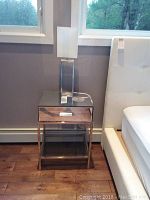 Front view of side table and lamp placed beside a bed