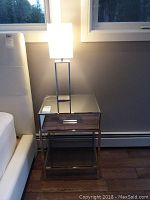 Front view of side table and lamp showing mirrored top, drawer front and lower shelf