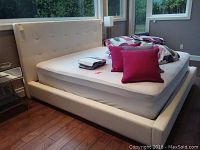 Full view of white faux leather king bed frame with mattress in room