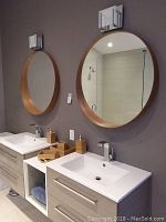 Two round wooden mirrors mounted above bathroom sinks with wooden accessories on counters