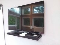 Front view of TV mounted above floating shelf with manual and box on shelf