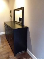 Full side angle view of the dark pine 8-drawer dresser with the matching mirror resting on top against a wall.