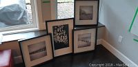 Three black and white framed prints of various sizes displayed on dark flooring near a wall.