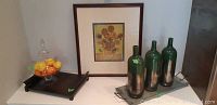 Framed Van Gogh Sunflowers print on wall. Brown tray below with pedestal bowl containing artificial fruit on top. Three green bottles on metallic tray to the right.