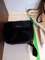 Black rectangular Bushnell carrying case positioned on a shelf corner, with flap closed, textured fabric.