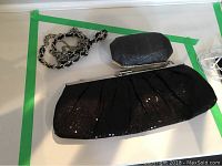 Small hexagonal black textured evening clutch with silver frame alongside larger black sequined evening clutch