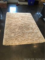 Full view of cream-colored high-pile IKEA Gaser rug laid flat on polished dark grey floor showing size and shape.
