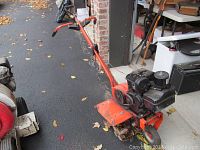 Full side view showing the entire zinck roto tiller and its orange frame, blade cover, tines, and black gas engine with wear marks.