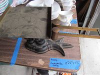 View of entire Fairbanks scale from left side showing scale pan, weights, and base on a wooden table with plates and cups in background.