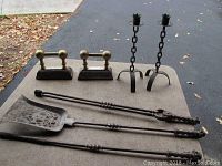 Full set shown on outdoor surface including two wrought iron candlesticks with chain design, two brass-accented tool rests, and three fireplace tools (poker, tongs, shovel)