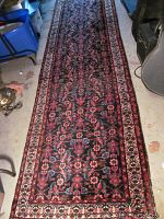 Full view of long Persian runner rug showing overall pattern and colors; placed on a concrete floor surrounded by various items.