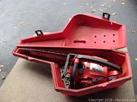 Chainsaw inside its red plastic carrying case showing overall shape and case condition.