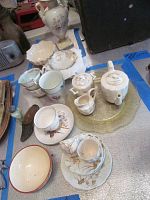Photo showing partial child's tea set with teapot, creamer, sugar bowl, cups, and saucers, depression glass plate beneath, RS Prussia vase in background.