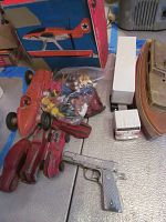 Overview of collection showing wooden tin wind-up boat, red vintage metal toy cars, white and red toy truck, silver toy gun, and bag of plastic figurines.