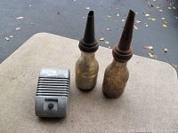 Original vintage drive-in movie speaker and two old glass oil bottles with metal spouts on outdoor surface, showing overall lot contents