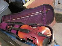 Violin and bow placed inside the purple-lined case showing the violin with strings and bow hair missing.