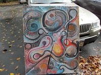 Front view of large abstract oil painting with vibrant swirling shapes and lines on canvas in outdoor setting.