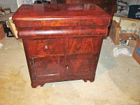 Front view of the 19th century flame mahogany dry sink showing the single drawer above the cabinet door with a crack and repaired area.
