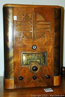 Front view of wood veneer tombstone style radio with carved speaker grille and glass dial
