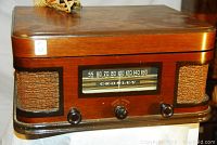 Front view of wood cabinet radio-turntable with cloth speaker grilles, central AM dial and control knobs, power cord on top