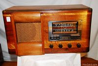 Front angle showing wooden cabinet, speaker grille with fabric cover, control knobs, and radio dial with RCA Victor branding.