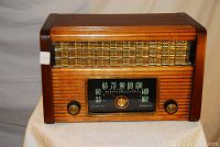 Front view showing wooden cabinet, woven speaker grille, tuning dial with frequencies, and two tuning knobs.
