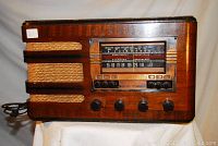 Front view showing wood cabinet, woven grille, tuning window, push-buttons and knobs