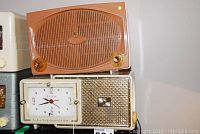 Wide view showing Bulova clock radio with gold-tone speaker grille and white clock face below the orange-brown Zenith radio.