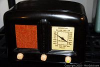Front view of the Westinghouse WR120 vintage radio showing speaker grille with orange textured cloth on the left, tuning dial on the right with numeric frequency display for broadcast and police bands, and three ivory tuning knobs below.