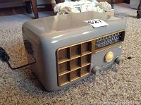 Side angled view of grey plastic radio with gold speaker grille, three front knobs, and tuning dial window showing frequency bands.