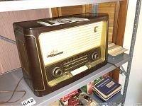 Front and side overview of brown bakelite tabletop radio on metal shelf