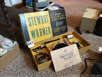 Original yellow and black cardboard box labeled Stewart Warner Deluxe Allwave Antenna containing boxed components including antenna rods, cables, and accessories arranged inside