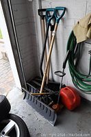 Photo showing two snow shovels, black weed eater, red gas container, and green hose